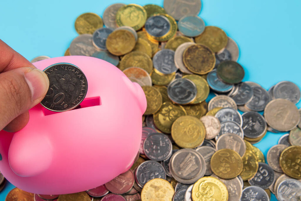 Man put Coins with piggy bank on blue background -Saving Concept. - Photo, Image