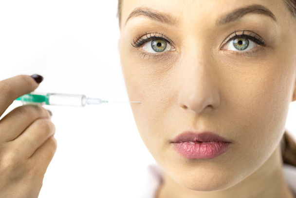 Young woman filling female wrinkles on cheek with hyaluronic acid from syringe - Photo, Image