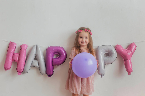 cute little girl in a pink dress posing in front of the camera. Smiling beautiful girl with long hair on a white background with balloons, copy space, headshot - Valokuva, kuva