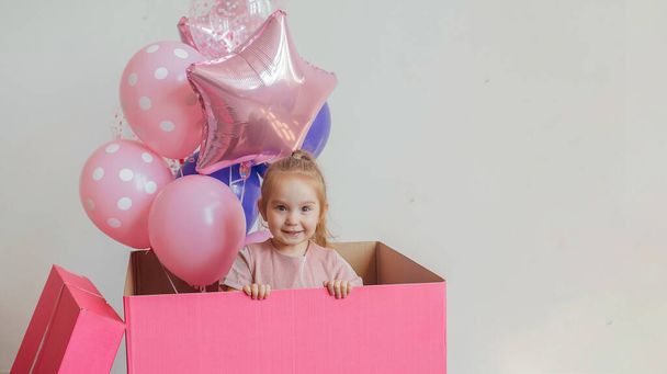 little beautiful girl in a big pink gift box with balloons - Foto, Bild