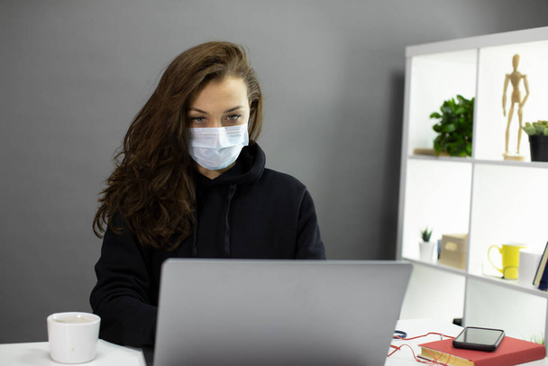 Young beautiful freelancer works remotely with face mask, quarantine concept - 写真・画像