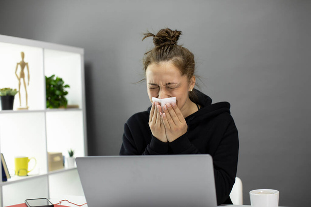 chora młoda kobieta siedzi przy komputerze w domu biuro, czuje się źle i kicha - Zdjęcie, obraz