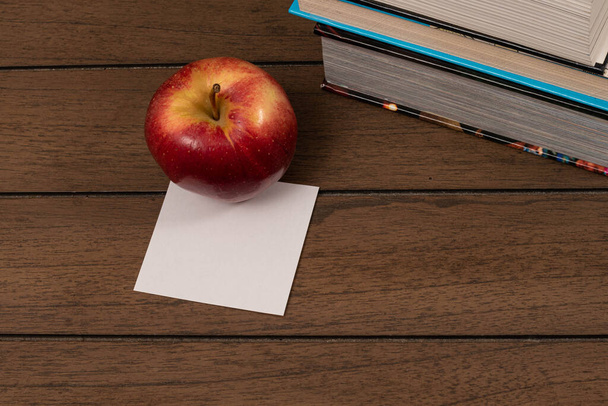 Rode appel met een briefpapier en wat boeken op een houten ondergrond - Foto, afbeelding