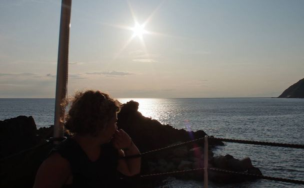 kavkazská blondýnka sledující plachetnici na obzoru při západu slunce v plážovém baru - Fotografie, Obrázek
