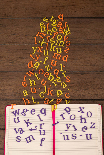 Otevřít zápisník s fialovými plastovými písmeny a žlutými a oranžovými písmenky na dřevěném pozadí - Fotografie, Obrázek