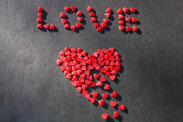 Összetört szív, boldogtalan szerelem. Egy nagy vörös szív kis darabokból áll. Fentről a szerelem szó kicsi szívekből áll.. - Fotó, kép