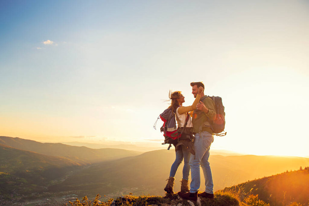 feliz casal homem e mulher turista no topo da montanha ao pôr do sol ao ar livre durante uma caminhada no verão
 - Foto, Imagem