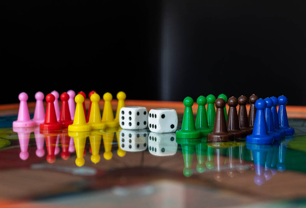 Closeup na staré bílé kostky s barevnými pěšáky nad deskovou hru s obytnými byty na pozadí - Fotografie, Obrázek