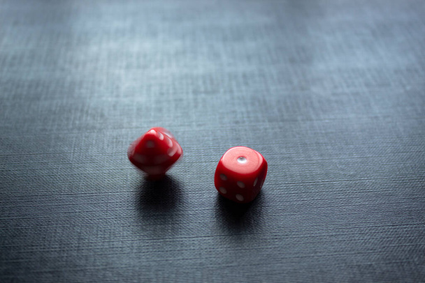 Closeup to a red dices, one dice is spinning over a black background. Ideal fo gamble, board games and bets - Photo, Image