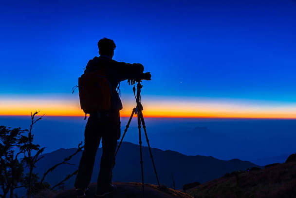 Sylwetka fotografa fotografuje krajobraz na szczycie góry, podczas gdy słońce zachodzi. Koncepcja inspiracji podróży - Zdjęcie, obraz