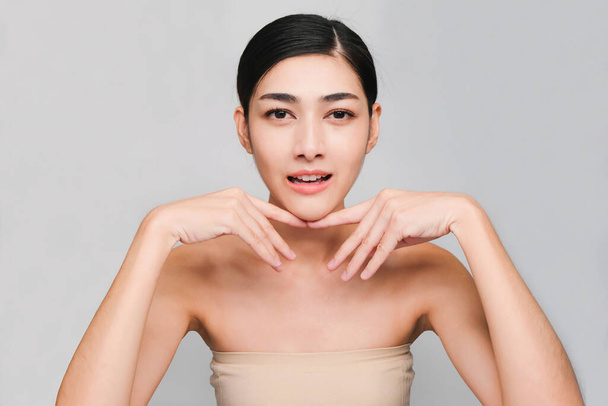 young beautiful asian woman with clean fresh skin, hands touch on the cheek, smiling and friendly,face care, facial treatment, Cosmetology, beauty and spa,isolated on grey background - Photo, image