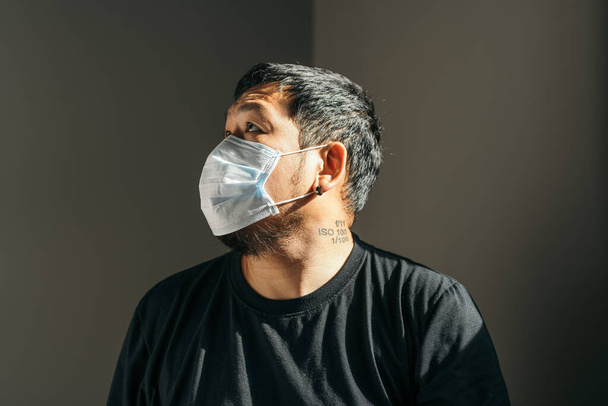 Asyalı adam koruyucu maske takıyor ve eve bakıyor. Corona Virüsü kavramı. Boşluğu kopyala. - Fotoğraf, Görsel