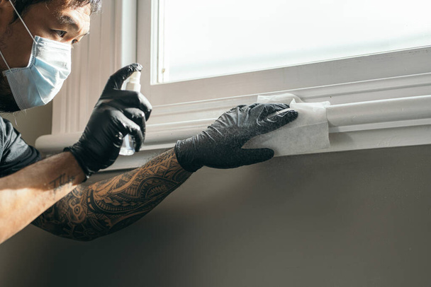 Koronavírus. Orvosi védőmaszkot viselő férfi és latex kesztyű takarítja a házat papírtörlőkkel és spray-vel, hogy megakadályozza a Coronavirus, Covid-19, influenza. Permetező üveg. Vírus és betegségvédelem. Kibaszott kéz a kézben. - Fotó, kép