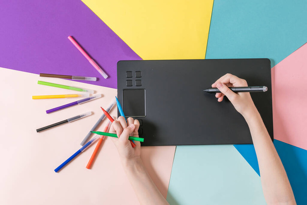 Handen met een set gekleurde markers en een grafische tablet op een veelkleurige papieren achtergrond. - Foto, afbeelding