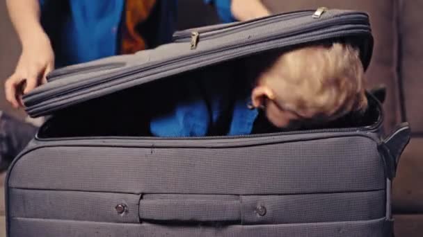 Two cute boys are playing with grey suitcase in the room at home. One little kid is inside the big valise and another boy is closing it. - Metraje, vídeo