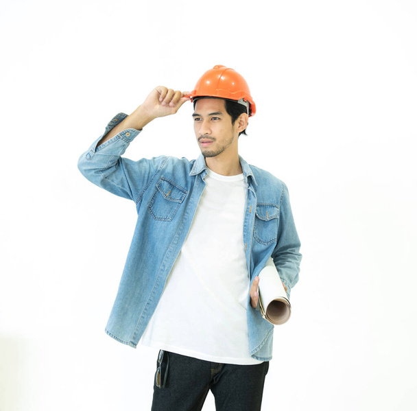 Aziatisch jong architect man hand aanraken oranje kleur hardhat weg te kijken terwijl het houden van blauwdrukken geïsoleerd op witte achtergrond in studio shot. - Foto, afbeelding