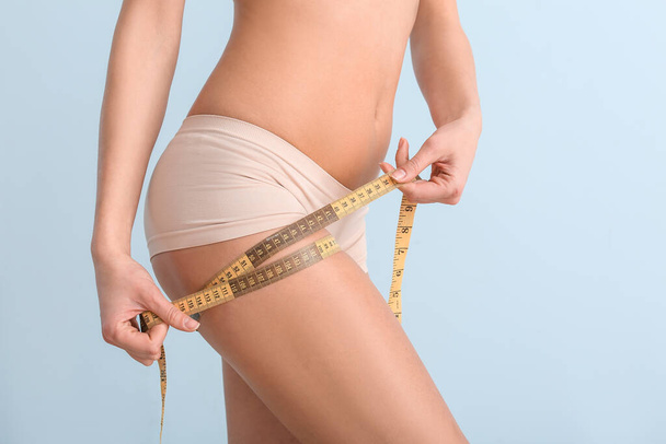 Young woman with measuring tape on color background. Concept of cellulite - Φωτογραφία, εικόνα
