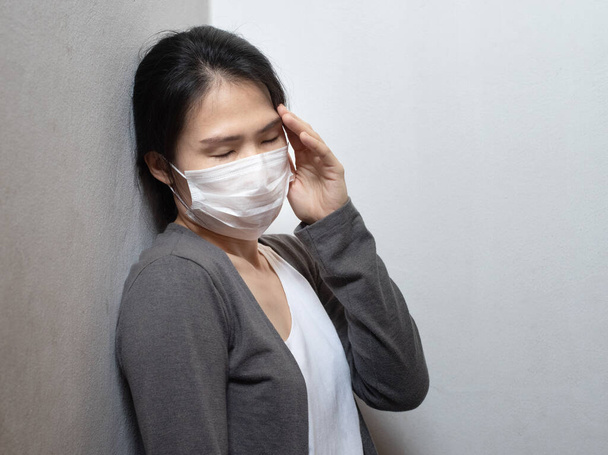 Female Asian young woman wearing surgical mask feeling sick headache and coughing leaning on wall isolated on white background.Wuhan coronavirus (COVID-19) pandemic prevention. Health care concept - Фото, изображение