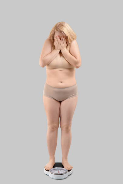 Trieste vrouw met overgewicht met schubben op grijze achtergrond. Gewichtsverlies concept - Foto, afbeelding