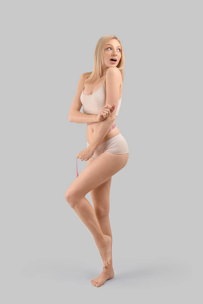 Slanke vrouw met meetlint op grijze achtergrond. Gewichtsverlies concept - Foto, afbeelding
