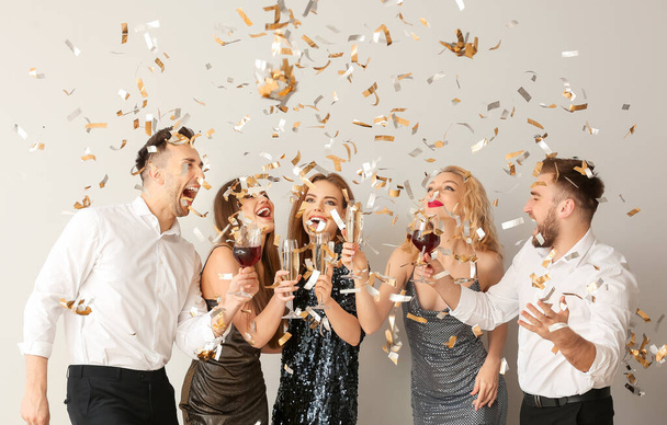 Szczęśliwi ludzie z kieliszkami napojów alkoholowych i konfetti na szarym tle - Zdjęcie, obraz