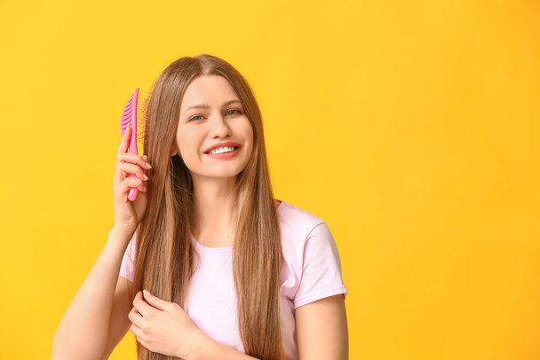Beautiful young woman brushing hair on color background - Photo, Image