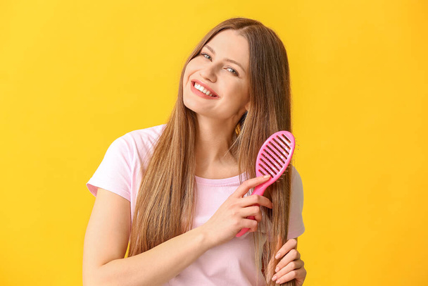 Beautiful young woman brushing hair on color background - Fotó, kép