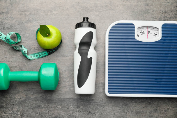 Weight scales with measuring tape, bottle of water, apple and dumbbell on grey background. Slimming concept - Photo, Image