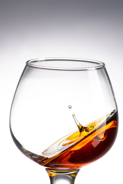 drop falling in a round glass with cognac or whiskey, a splash at an amazing angle - Fotoğraf, Görsel