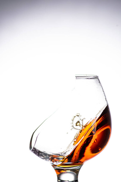 a drop falling into a glass with a broken wall with cognac or whiskey, a splash at an amazing angle - Фото, зображення