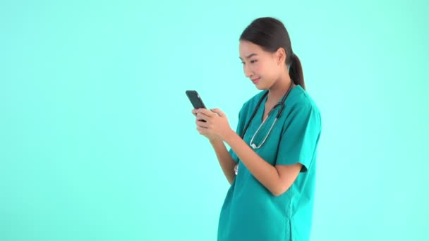 Portrait beautiful young asian doctor woman using smartphone on blue isolated background - Filmati, video