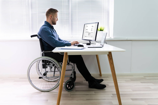 Gehandicapte zakenman zit op een rolstoel en gebruikt computer op kantoor - Foto, afbeelding