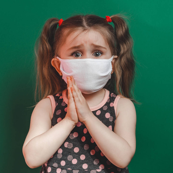 コロナウイルス流行中の医療マスクの白人病の少女は、緑の背景のクローズアップで祈ります2021 - 写真・画像
