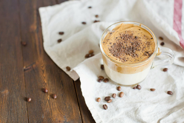 Iced Dalgona Koffie met chocolade poeder in een glazen beker. Trendy pluizige romige opgeklopte koffie. Koffie op een houten achtergrond - Foto, afbeelding