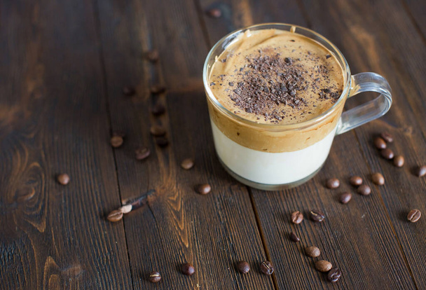 Mrożona kawa Dalgona z czekoladowym proszkiem w szklanym kubku. Modna puszysta, puszysta, bita kawa. Kawa na drewnianym tle - Zdjęcie, obraz