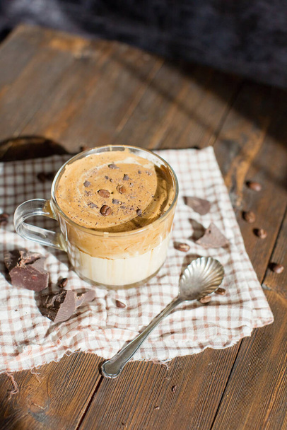 Παγωμένος καφές Dalgona με σκόνη σοκολάτας σε γυάλινο κύπελλο. Μοντέρνο αφράτο κρεμώδες χτυπημένο καφέ. Καφές σε ξύλινο φόντο - Φωτογραφία, εικόνα