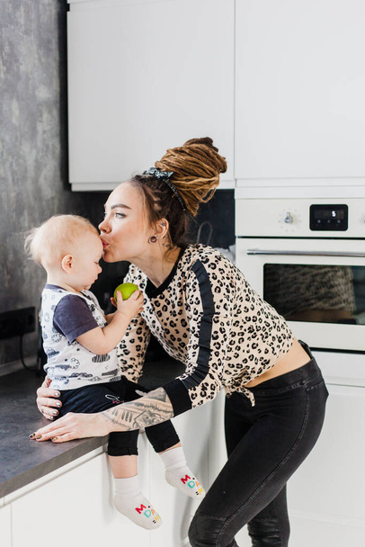 Μαμά και το μωρό μιλούν, στο σπίτι στην κουζίνα, κορίτσι και dreadlocks, Μήλο, υγιεινή τροφή για το παιδί, - Φωτογραφία, εικόνα