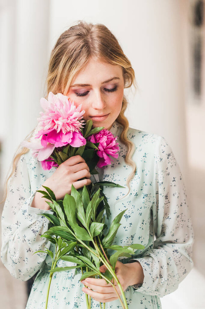 A girl with long blonde hair and beautiful flowers, peonies, in a light dress, a walk in the park, summer and spring, beauty and fashion - 写真・画像
