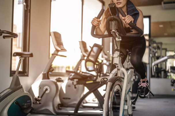 Front view of woman workout with bike. Women exercise working out in the gym for healthy lifestyle on bike at sunset. fitness ,workout, gym exercise ,lifestyle  and healthy concept.  - Foto, Bild