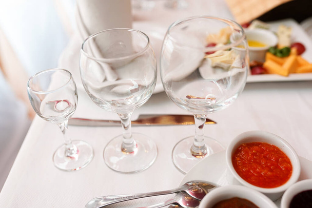 Ravintola pöytä asettaa lasit viiniä, lautasliinat ja ruokailuvälineet. Lasit ravintolassa. Pöydän kattaminen juhla loma ruokaa, juomia ja koristelu. Tarjouskukan kukat
. - Valokuva, kuva