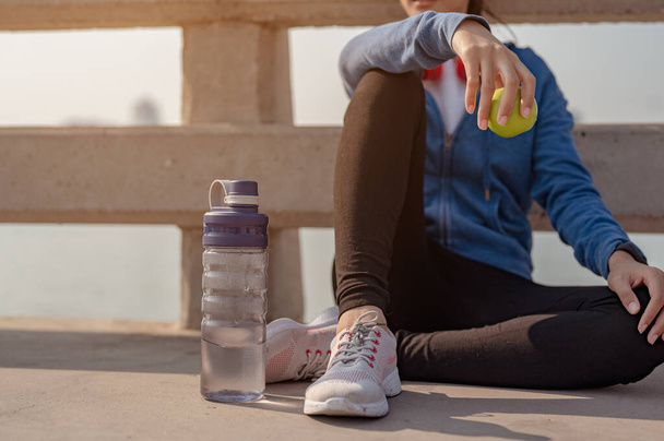 Young woman drink water and sitting to rest after jogging a morning workout in the city. A city that lives healthy in the capital. Exercise, fitness, jogging, running, lifestyle, healthy concept. - Foto, Imagem