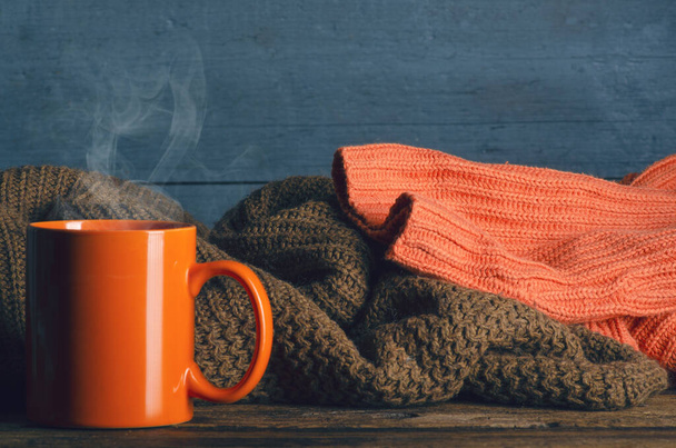 Pile of knitted warm clothes and cup mug tea on wooden background, sweaters, knitwear - Foto, Imagem