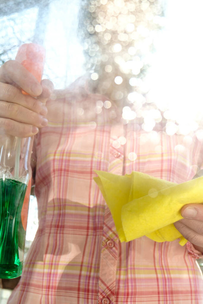 Nainen pesee ikkunalasin pölystä ja liasta käyttäen suihketta pesuaineilla ja räteillä aurinkoisena kevätpäivänä. Puhtauden käsite
. - Valokuva, kuva