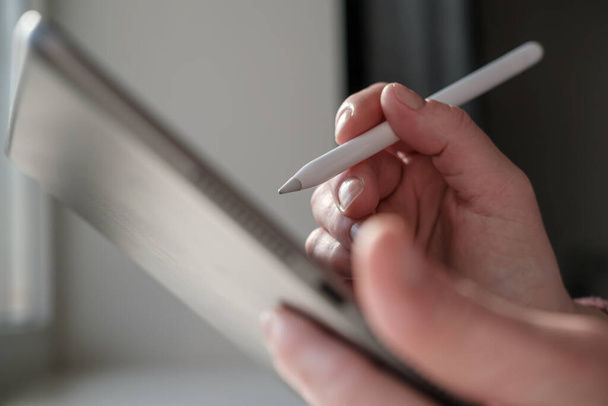 Hand schrijft of tekent met stylus pen op een digitale tablet, thuis. Close-up. - Foto, afbeelding
