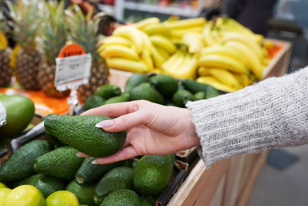 Cropped image of a customer choosing avocados in the supermarket. close up of woman hand holding avocado in market. sale, shopping, food concept - Valokuva, kuva