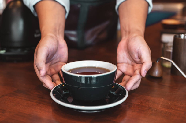 Close up of hands barista man serving coffee in coffee shop. male hands placing a cup of coffee on table. Coffee, Barista, extraction, serve, cafe, lifestyle concept. - Photo, image