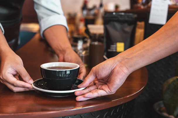 Close up of hands barista man serving coffee in coffee shop. male hands placing a cup of coffee on table. Coffee, Barista, extraction, serve, cafe, lifestyle concept. - Foto, imagen