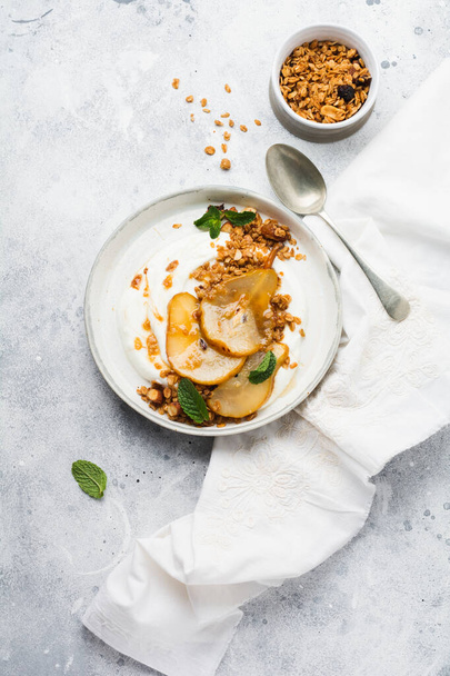 Greek yogurt with caramelized pear, granola, nuts and melted sugar for a wholesome breakfast on a gray ceramic plate. Rustic style. Top view. - Foto, Imagen