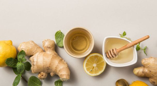 Ginger Lemon Tea with Honey. Warming immune boosting tea with citrus and ginger. Cup, honey,  ginger root on grey  pastel background, copy space, top view. - Foto, immagini