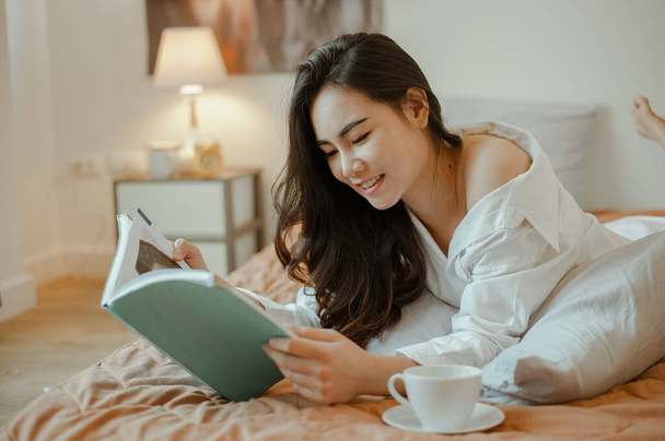 Young woman asia living at home relaxing and reading a book in the bedroom on holiday. Asian, asia, relax, alone, technology, lifestyle concept. - Photo, Image